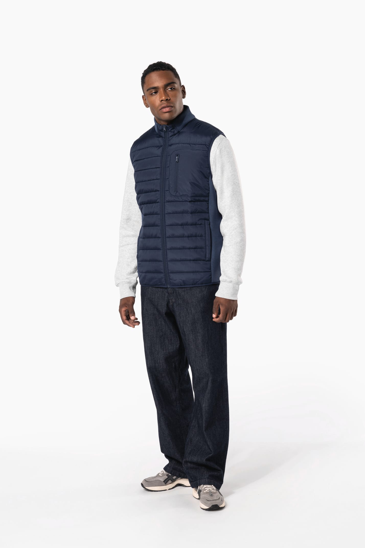 Jeune homme brun cheveux courts qui porte un bodywarmer bi matière bleu marine brillant.