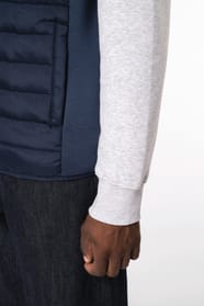 Jeune homme brun cheveux courts qui porte un bodywarmer bi matière bleu marine brillant.