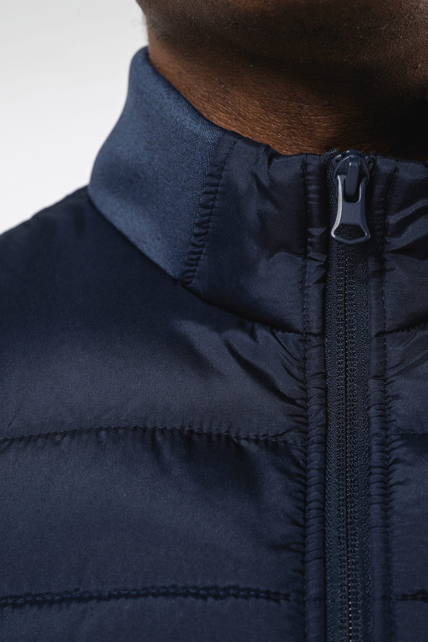 Jeune homme brun cheveux courts qui porte un bodywarmer bi matière bleu marine brillant.