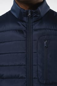 Jeune homme brun cheveux courts qui porte un bodywarmer bi matière bleu marine brillant.