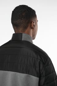 Jeune homme brun cheveux courts qui porte une veste bi matière noire et grise.