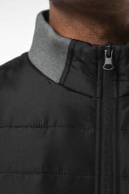 Jeune homme brun cheveux courts qui porte une veste bi matière noire et grise.