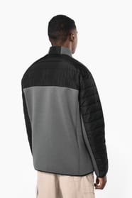 Jeune homme brun cheveux courts qui porte une veste bi matière noire et grise.
