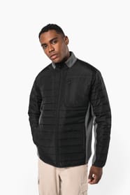 Jeune homme brun cheveux courts qui porte une veste bi matière noire et grise.
