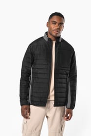 Jeune homme brun cheveux courts qui porte une veste bi matière noire et grise.