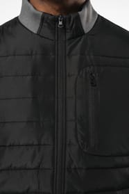 Jeune homme brun cheveux courts qui porte une veste bi matière noire et grise.