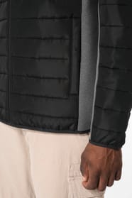 Jeune homme brun cheveux courts qui porte une veste bi matière noire et grise.