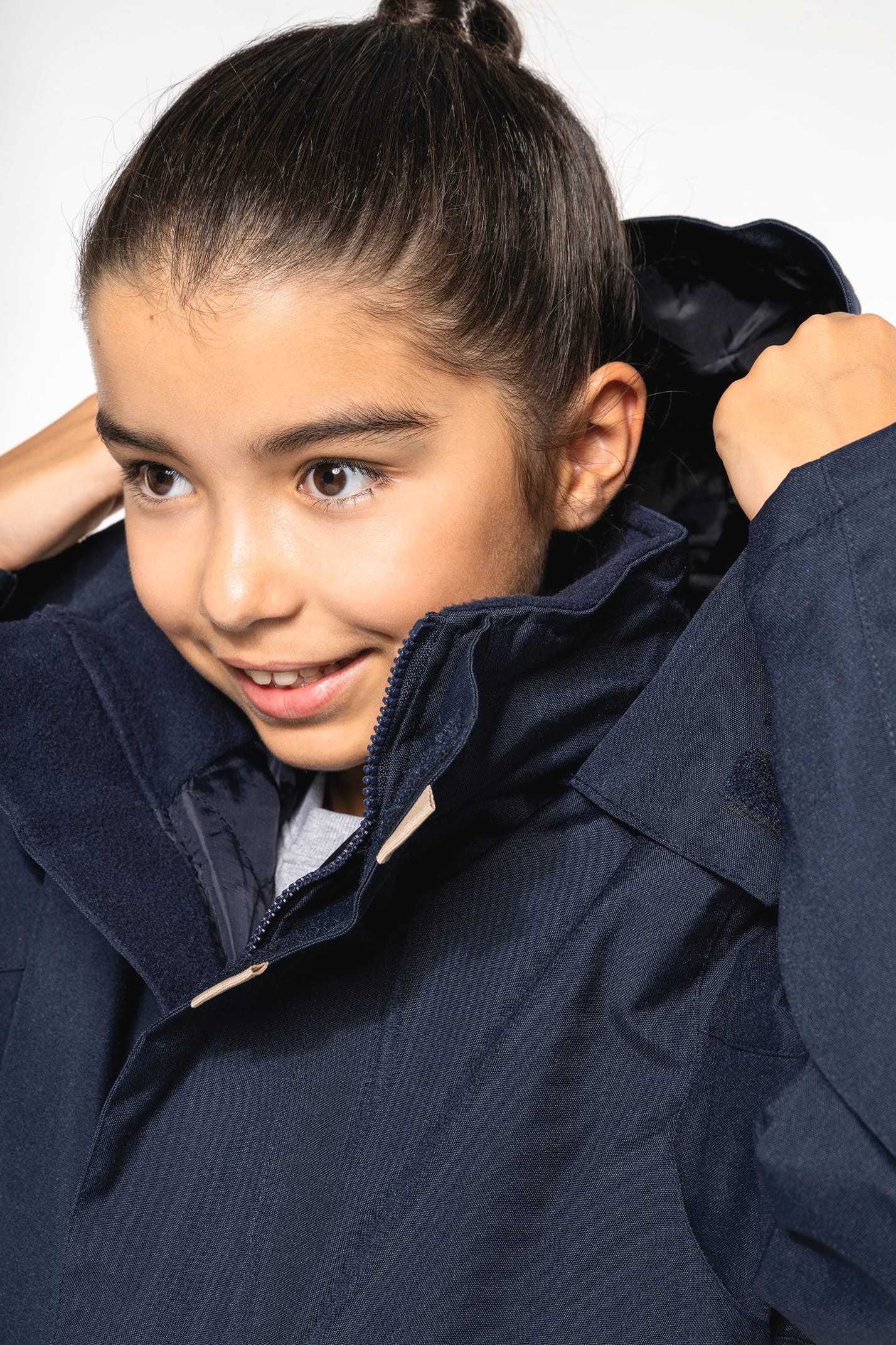 Jeune fille brune cheveux attachés qui porte une parka Navy.