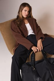 Jeune femme blonde aux cheveux longs avec un sac de voyage noir assise sur un fauteuil camel.