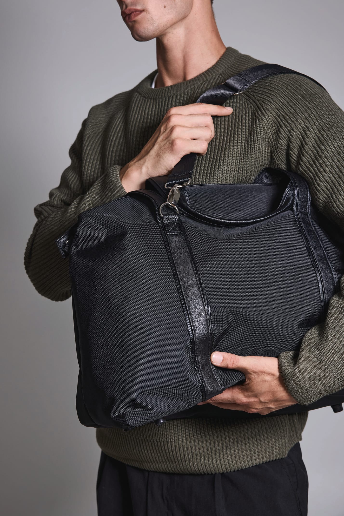 Jeune homme debout qui tient fermement  un sac de voyage noir.