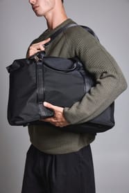 Jeune homme debout qui tient fermement  un sac de voyage noir.