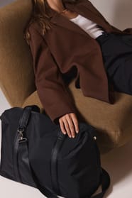 Jeune femme avec un sac de voyage noir assise sur un fauteuil camel.