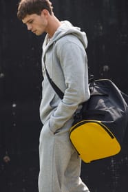 Jeune homme en jogging qui marche avec un sac de sport bicolore noir et jaune?