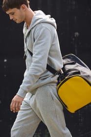 Jeune homme en jogging qui marche avec un sac de sport bicolore noir et jaune?