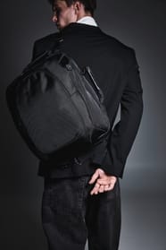 Homme habillé en noir dans une ambiance feutrée avec un sac à dos ordinateur noir.