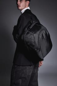 Homme habillé en noir dans une ambiance feutrée avec un sac à dos ordinateur noir.