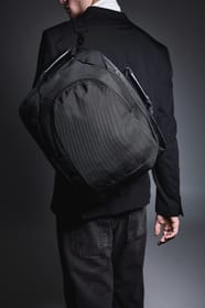 Homme habillé en noir dans une ambiance feutrée avec un sac à dos ordinateur noir.