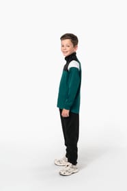 Jeune garçon qui porte une veste de survêtement zippée tricolore : verte, noire et blanche.