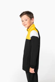 Jeune garçon qui porte une veste de survêtement zippée tricolore tendance et personnalisable : jaune, noire et blanche.
