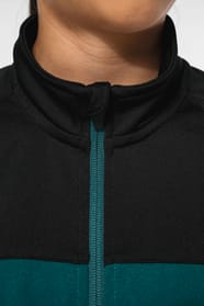 Jeune fille brune cheveux attachés qui porte une veste de survêtement zippée tricolore tendance et personnalisable : verte, noire et blanche.