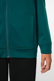 Jeune fille brune cheveux attachés qui porte une veste de survêtement zippée tricolore tendance et personnalisable : verte, noire et blanche.