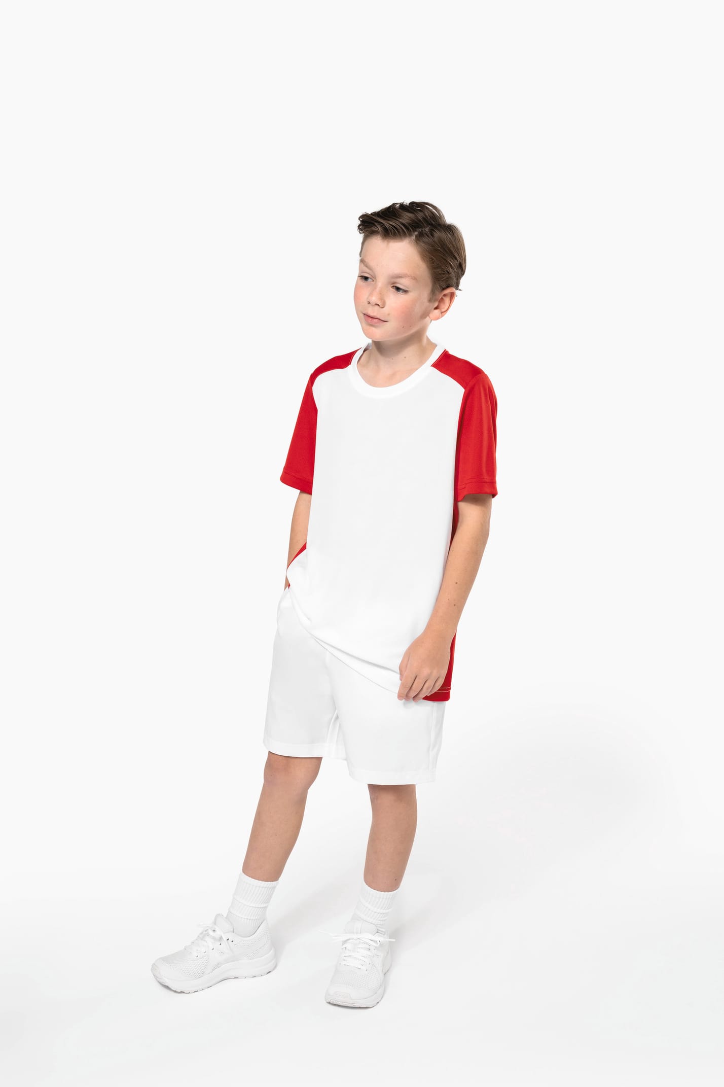 Jeune garçon châtain cheveux courts qui porte un t-shirt bicolore et un short de sport.