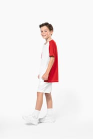Jeune garçon châtain cheveux courts qui porte un t-shirt bicolore et un short de sport.