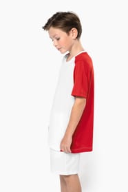 Jeune garçon châtain cheveux courts qui porte un t-shirt bicolore et un short de sport.
