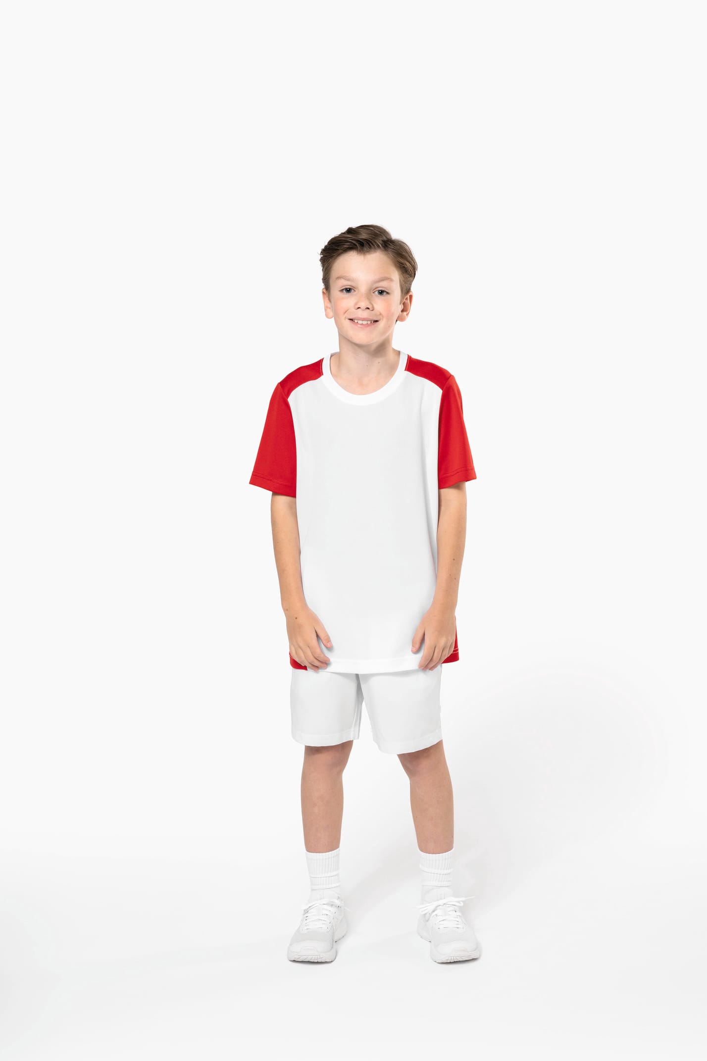 Jeune garçon châtain cheveux courts qui porte un t-shirt bicolore et un short de sport.