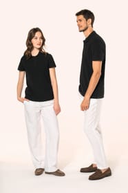 Jeune femme aux cheveux châtains longs et légèrement ondulés, et jeune homme aux cheveux châtains courts portent chacun un polo noir en coton Supima® à manches courtes, sobre et élégant. Sa fibre extra-longue apporte résistance et douceur, idéale pour le 