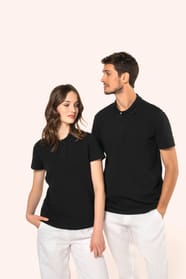 Jeune femme aux cheveux châtains longs et légèrement ondulés, et jeune homme aux cheveux châtains courts portent chacun un polo noir en coton Supima® à manches courtes, sobre et élégant. Sa fibre extra-longue apporte résistance et douceur, idéale pour le 