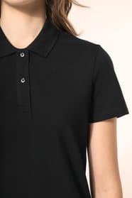 Jeune femme aux cheveux châtains longs et légèrement ondulés, portant un polo noir en coton Supima® à manches courtes, sobre et élégant. Sa fibre extra-longue offre résistance et douceur, idéale pour le marquage textile. Elle complète sa tenue avec un pan