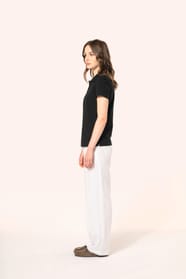 Jeune femme aux cheveux châtains longs et légèrement ondulés, portant un polo noir en coton Supima® à manches courtes, sobre et élégant. Sa fibre extra-longue offre résistance et douceur, idéale pour le marquage textile. Elle complète sa tenue avec un pan