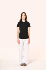 Jeune femme aux cheveux châtains longs et légèrement ondulés, portant un polo noir en coton Supima® à manches courtes, sobre et élégant. Sa fibre extra-longue offre résistance et douceur, idéale pour le marquage textile. Elle complète sa tenue avec un pan