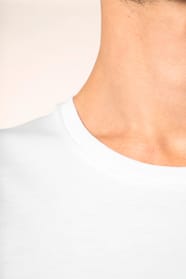Jeune homme aux cheveux châtains courts portant un T-shirt blanc en coton Supima® col rond à manches courtes, 180 g/m². Sa coupe droite, sa construction coupée-cousue et ses finitions soignées mettent en valeur un jersey de grande finesse, au toucher doux