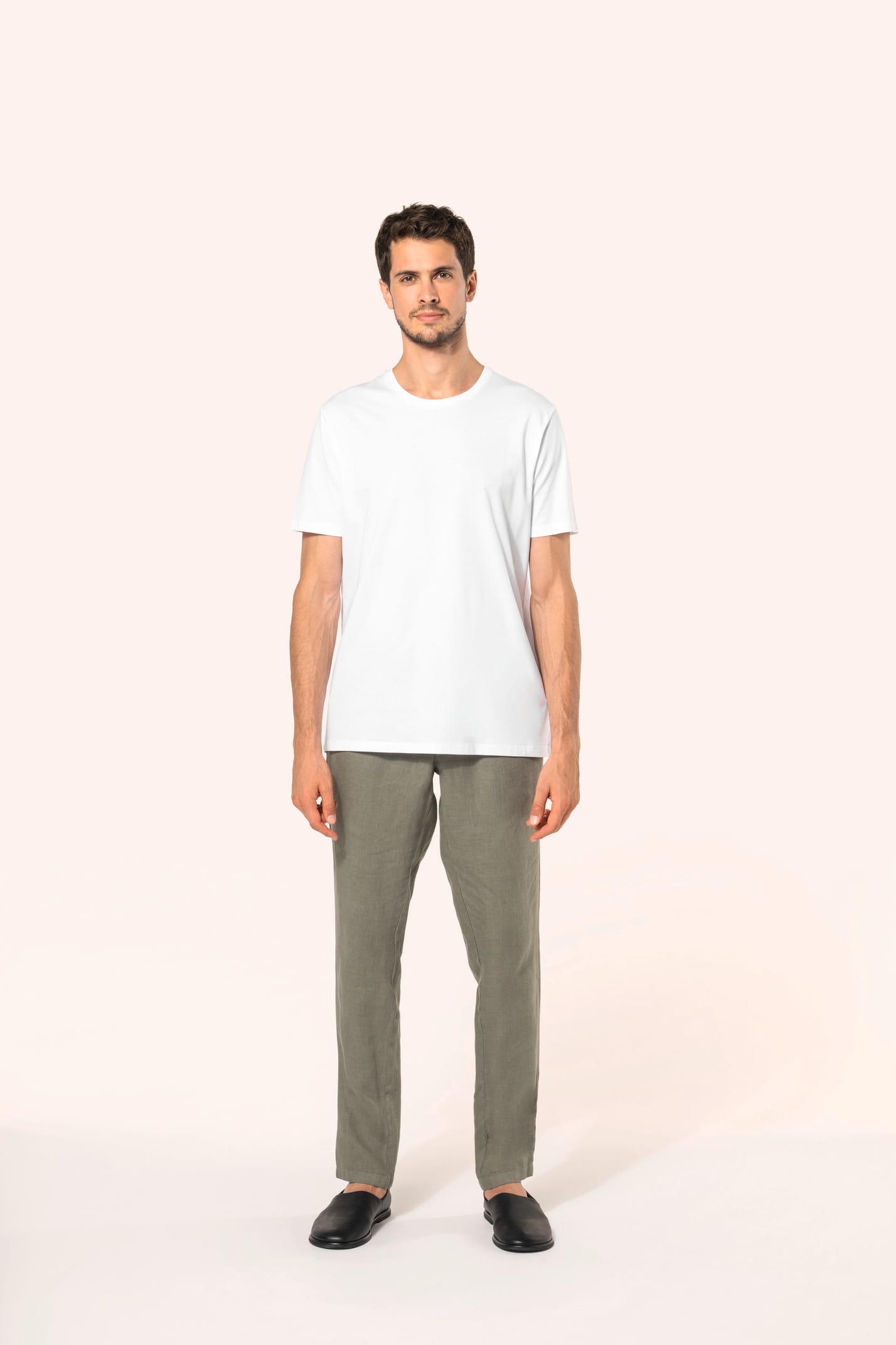 Jeune homme aux cheveux châtains courts portant un T-shirt blanc en coton Supima® col rond à manches courtes, 180 g/m². Sa coupe droite, sa construction coupée-cousue et ses finitions soignées mettent en valeur un jersey de grande finesse, au toucher doux