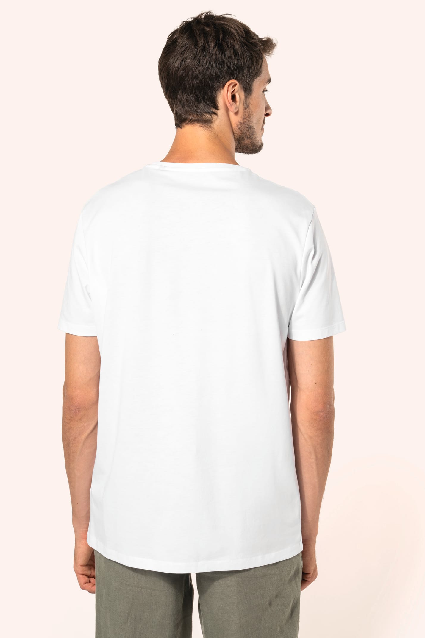 Jeune homme aux cheveux châtains courts portant un T-shirt blanc en coton Supima® col rond à manches courtes, 180 g/m². Sa coupe droite, sa construction coupée-cousue et ses finitions soignées mettent en valeur un jersey de grande finesse, au toucher doux