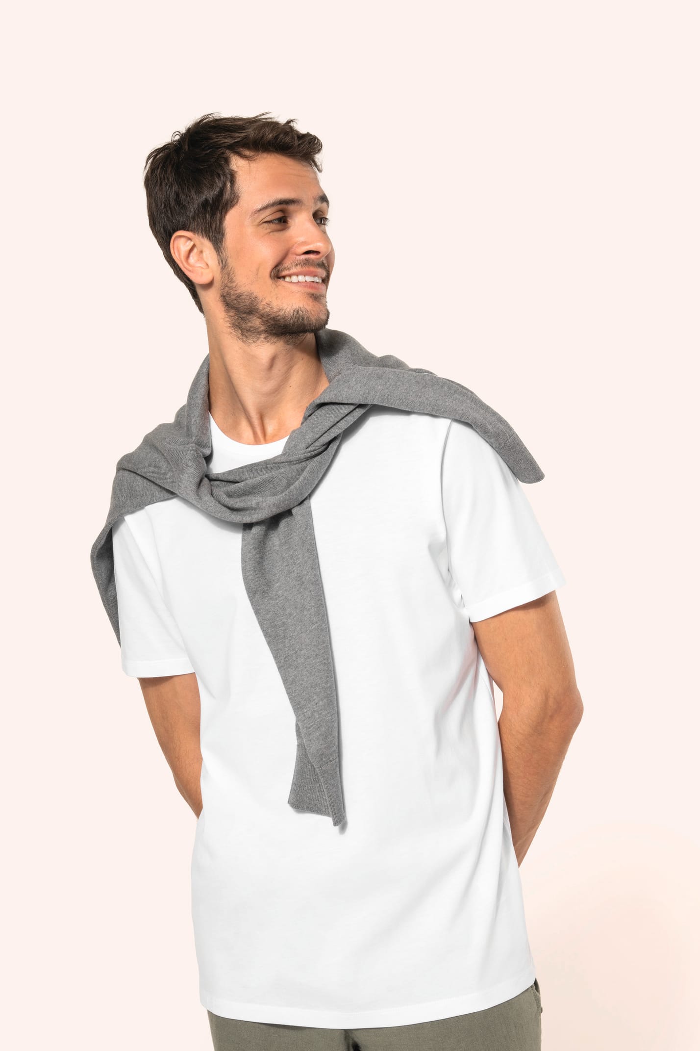 Jeune homme aux cheveux châtains courts portant un T-shirt blanc en coton Supima® col rond à manches courtes, 180 g/m². Sa coupe droite, sa construction coupée-cousue et ses finitions soignées mettent en valeur un jersey de grande finesse, au toucher doux