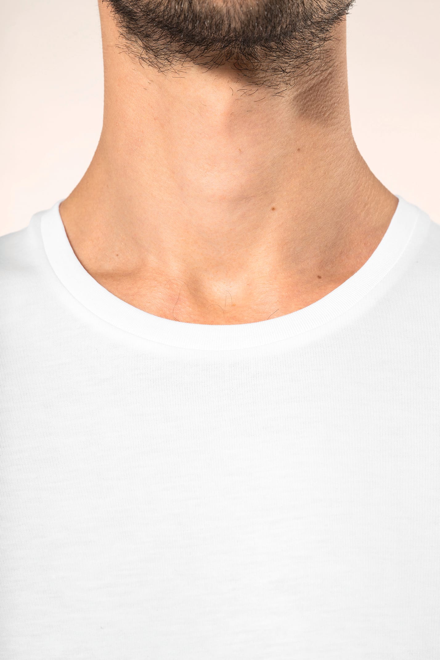 Jeune homme aux cheveux châtains courts portant un T-shirt blanc en coton Supima® col rond à manches courtes, 180 g/m². Sa coupe droite, sa construction coupée-cousue et ses finitions soignées mettent en valeur un jersey de grande finesse, au toucher doux