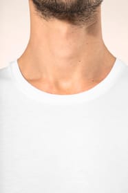 Jeune homme aux cheveux châtains courts portant un T-shirt blanc en coton Supima® col rond à manches courtes, 180 g/m². Sa coupe droite, sa construction coupée-cousue et ses finitions soignées mettent en valeur un jersey de grande finesse, au toucher doux