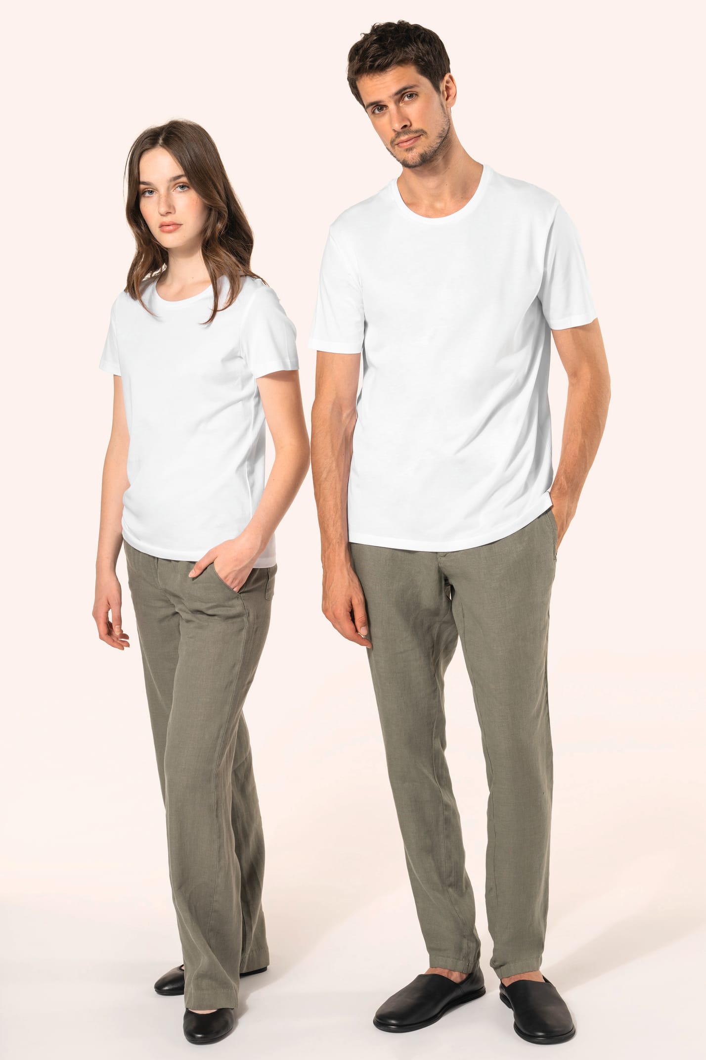 Jeune femme aux cheveux châtains longs et légèrement ondulés et jeune homme aux cheveux châtains courts portent un T-shirt blanc en coton Supima® col rond à manches courtes, 180 g/m². Associé à un pantalon en lin vert kaki clair, l’ensemble met en valeur 