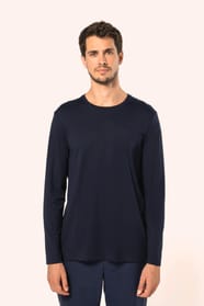 Jeune homme aux cheveux châtains courts portant un T-shirt bleu marine à manches longues en coton Supima® col rond, coupe droite, 180 g/m². Sa fibre extra-longue apporte résistance et douceur, tandis que les finitions soignées et la construction coupée-co
