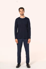 Jeune homme aux cheveux châtains courts portant un T-shirt bleu marine à manches longues en coton Supima® col rond, coupe droite, 180 g/m². Sa fibre extra-longue apporte résistance et douceur, tandis que les finitions soignées et la construction coupée-co