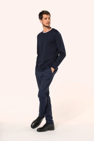 Jeune homme aux cheveux châtains courts portant un T-shirt bleu marine à manches longues en coton Supima® col rond, coupe droite, 180 g/m². Sa fibre extra-longue apporte résistance et douceur, tandis que les finitions soignées et la construction coupée-co