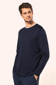 Jeune homme aux cheveux châtains courts portant un T-shirt bleu marine à manches longues en coton Supima® col rond, coupe droite, 180 g/m². Sa fibre extra-longue apporte résistance et douceur, tandis que les finitions soignées et la construction coupée-co
