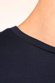 Jeune homme aux cheveux châtains courts portant un T-shirt bleu marine à manches longues en coton Supima® col rond, coupe droite, 180 g/m². Sa fibre extra-longue apporte résistance et douceur, tandis que les finitions soignées et la construction coupée-co