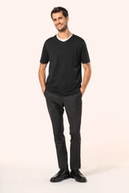 Jeune homme aux cheveux châtains courts portant un T-shirt noir à manches courtes en coton Supima® col V, coupe droite, 180 g/m². Sa fibre extra-longue apporte résistance et douceur, tandis que les finitions soignées et la construction coupée-cousue souli