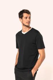 Jeune homme aux cheveux châtains courts portant un T-shirt noir à manches courtes en coton Supima® col V, coupe droite, 180 g/m². Sa fibre extra-longue apporte résistance et douceur, tandis que les finitions soignées et la construction coupée-cousue souli