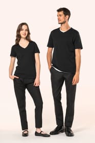 Jeune femme aux cheveux châtains longs et légèrement ondulés et jeune homme aux cheveux châtains courts portent chacun un T-shirt noir à manches courtes en coton Supima® col V, coupe droite, 180 g/m². Leur fibre extra-longue apporte résistance et douceur,