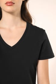 Jeune femme aux cheveux châtains longs et légèrement ondulés portant un T-shirt noir à manches courtes en coton Supima® col V, coupe droite, 180 g/m². Sa fibre extra-longue apporte résistance et douceur, tandis que les finitions soignées et la constructio